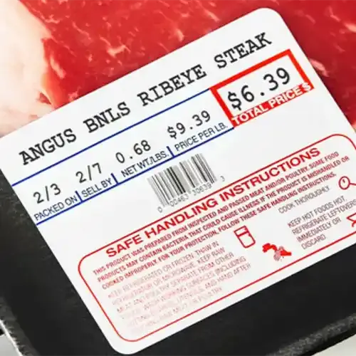 A scale-printed label on a tray of ribeye steak showing weight, price per pound, total price and safe handling instructions