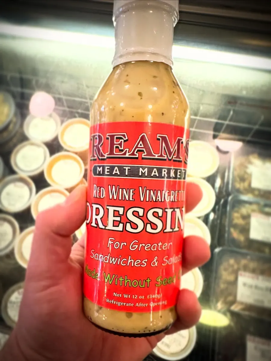 A hand holding a bottle of red wine vinaigrette dressing with a red printed label