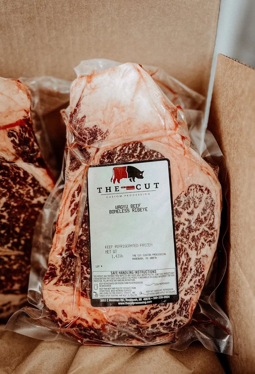 A vacuum-packed boneless ribeye in a shipping box with a branded label carrying the cut name and weight